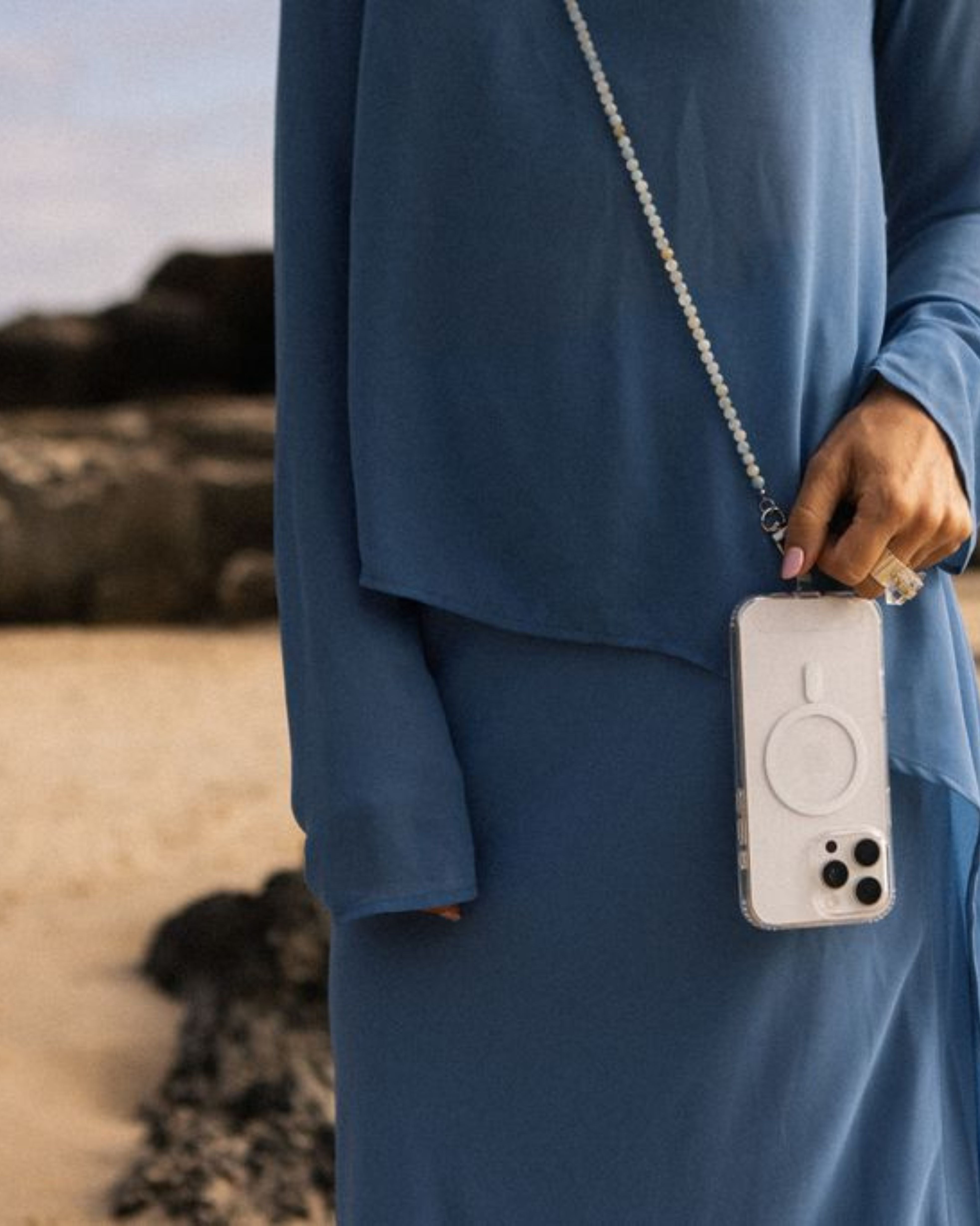 Person in a blue outfit holding a phone with a beige case against a natural background