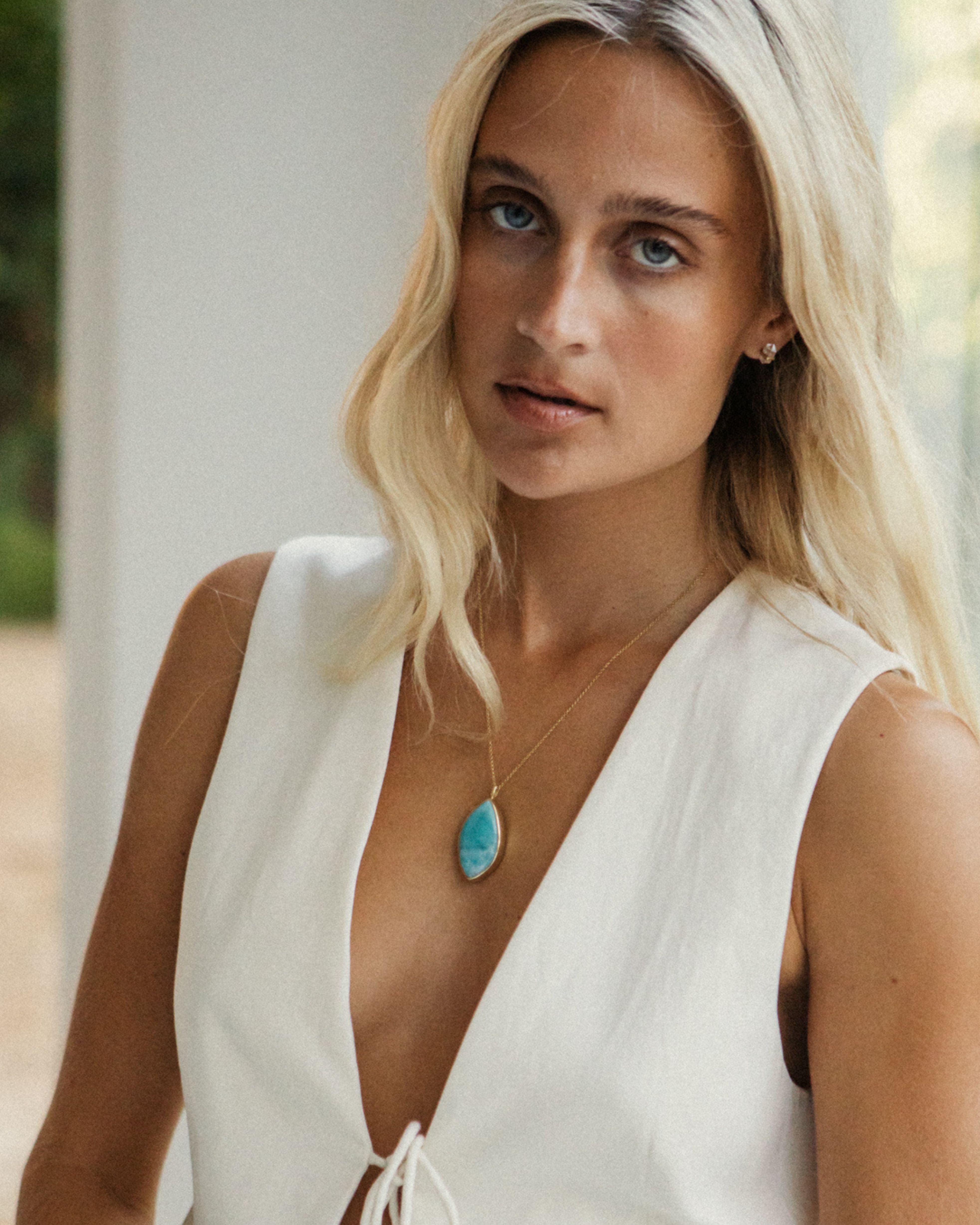 Woman wearing a white sleeveless top with a Larimar pendant necklace outdoors.