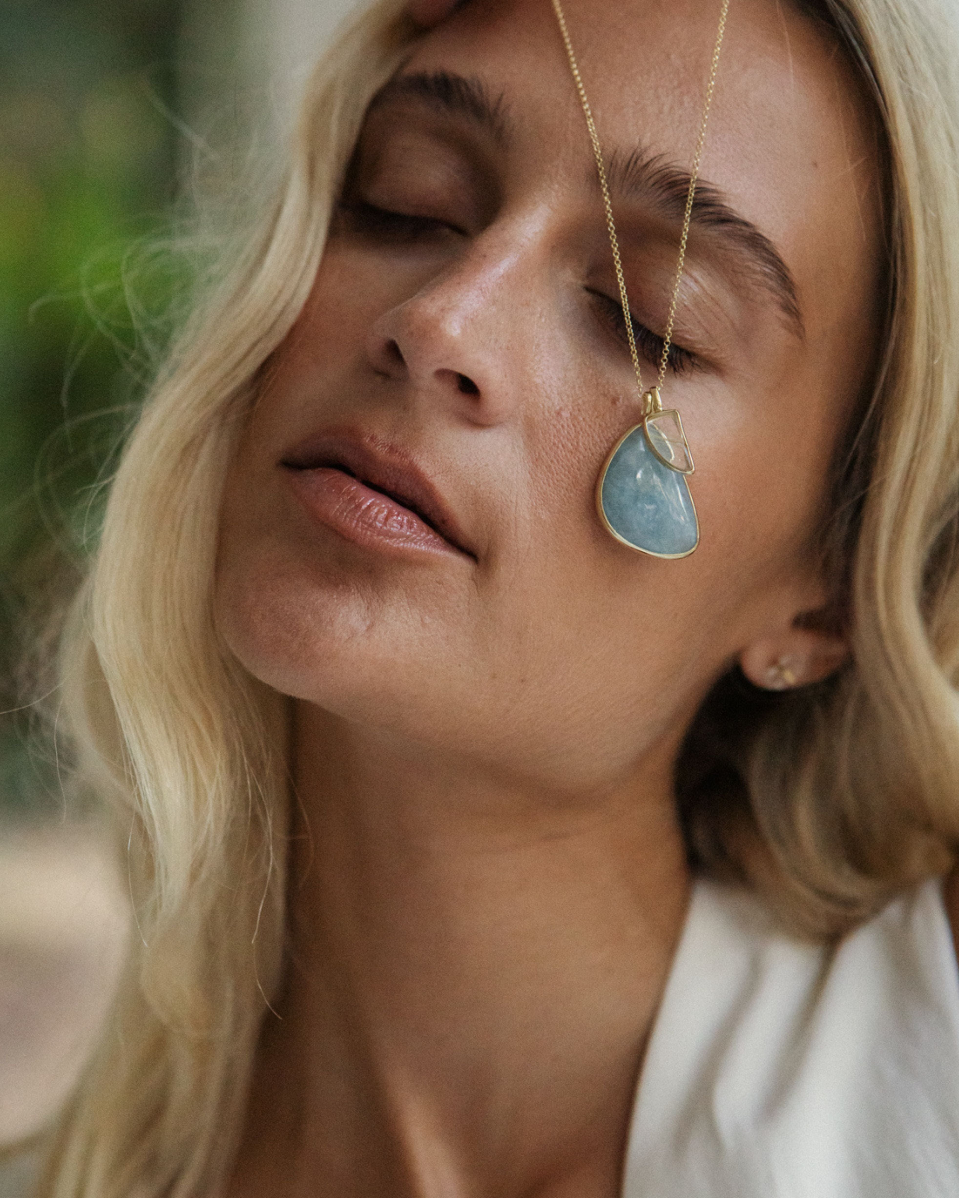 Close-up of a woman wearing a necklace with a teardrop-shaped Larimar + Rutilated Quartz pendant.