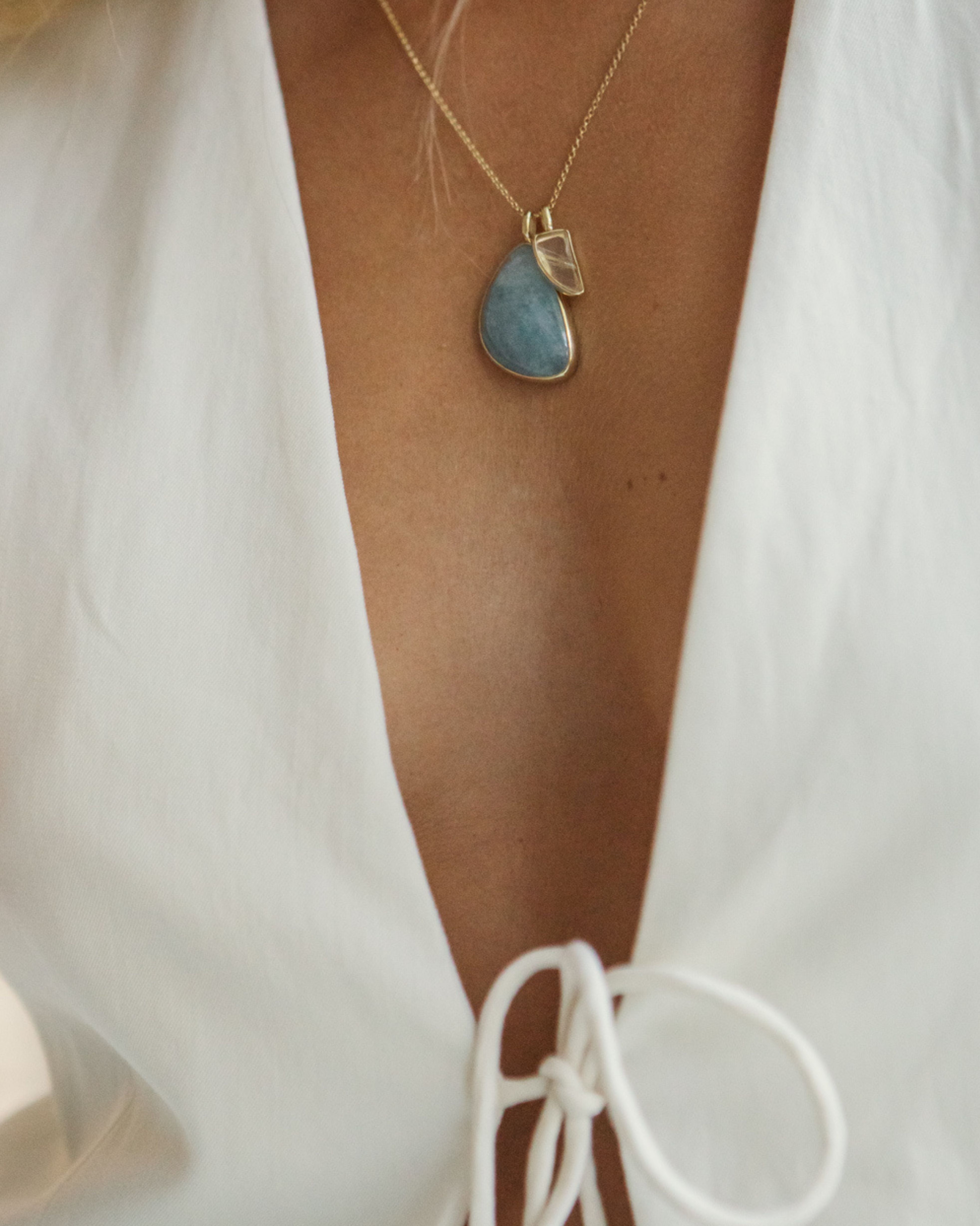 Necklace with a Larimar + Rutilated Quartz pendant worn by a person in a white outfit.