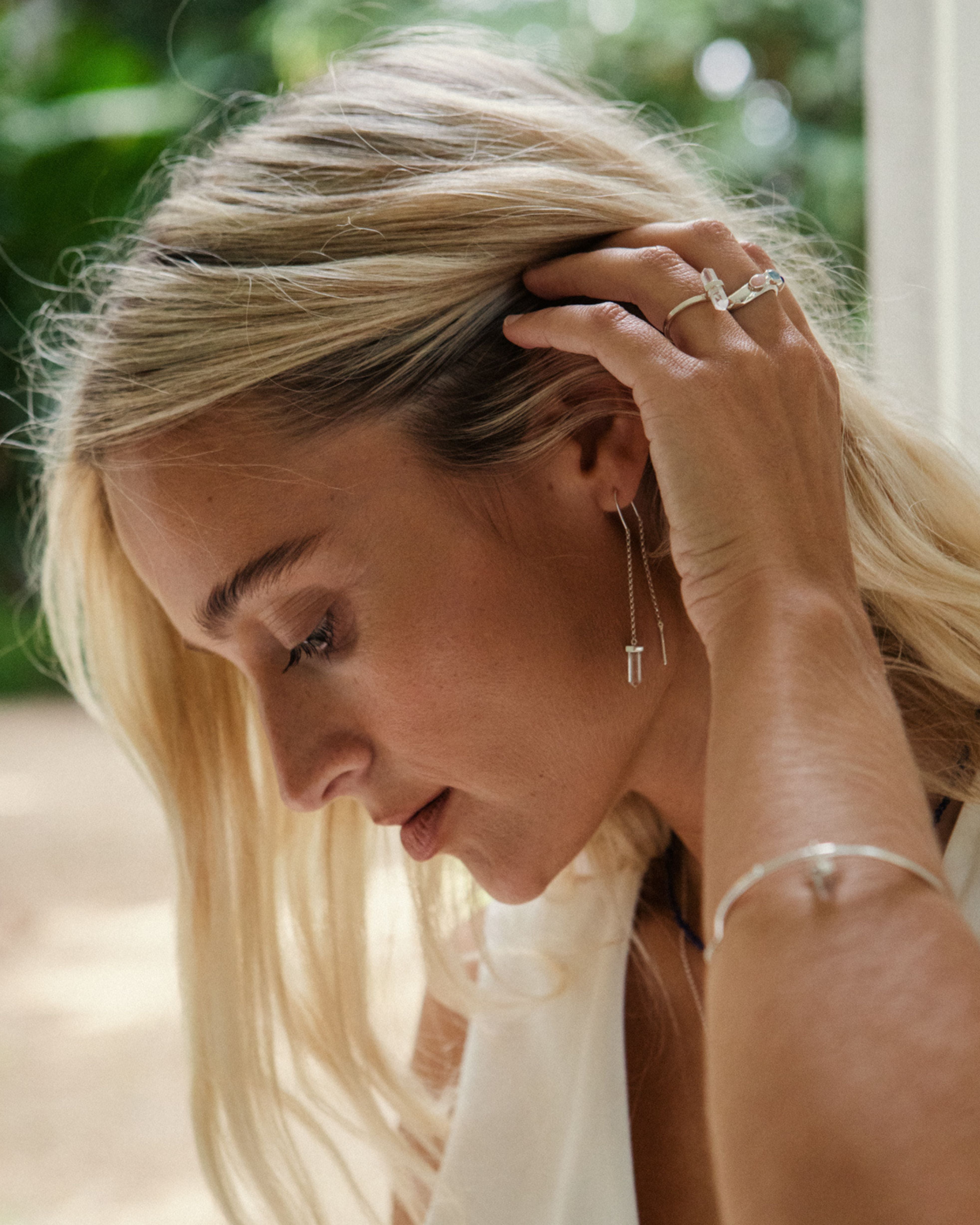 Woman adjusting her earrings with a blurred natural background