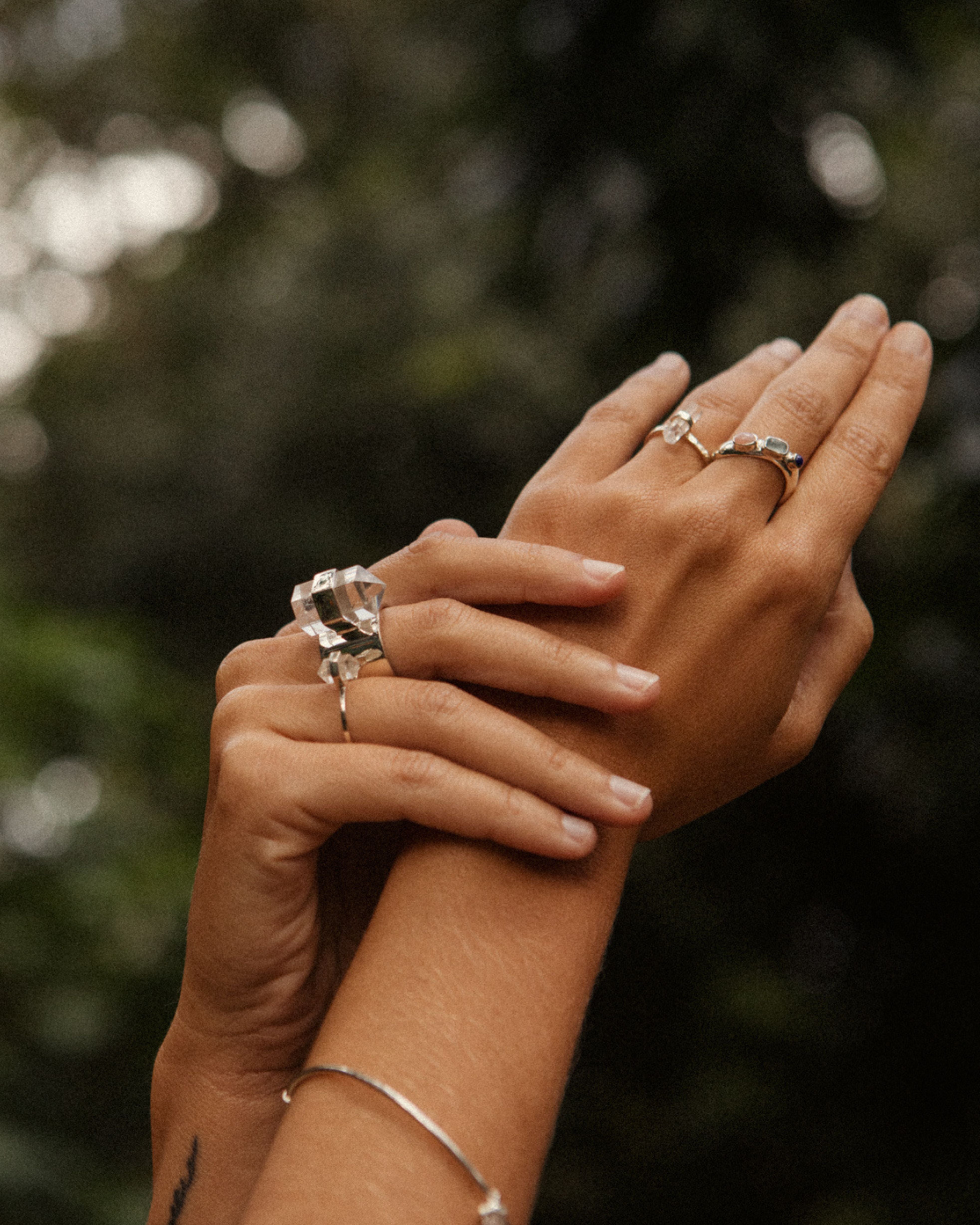 Close-up of two hands with rings against a blurred natural background