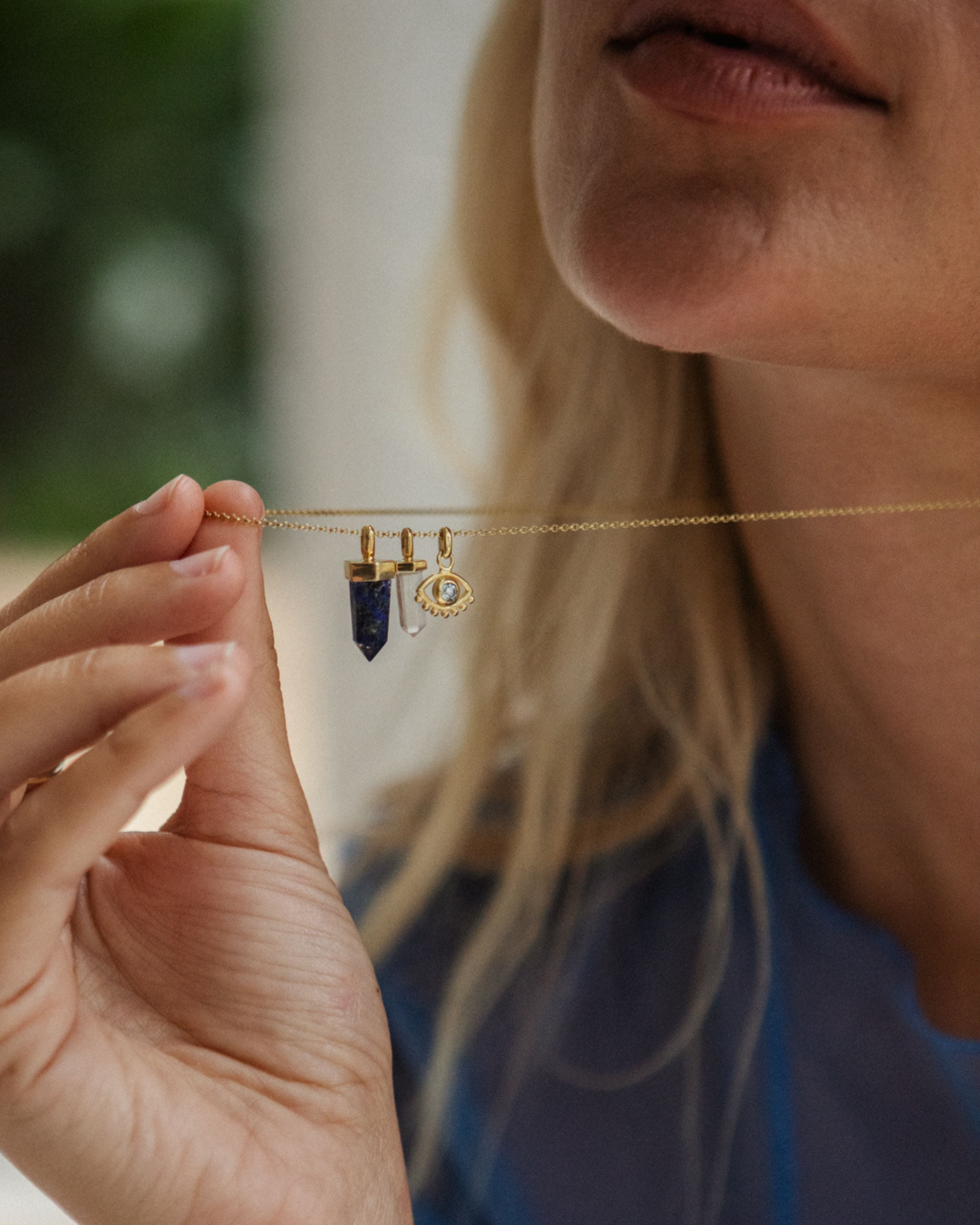 Person holding a gold necklace with gemstone pendants against a blurred background
