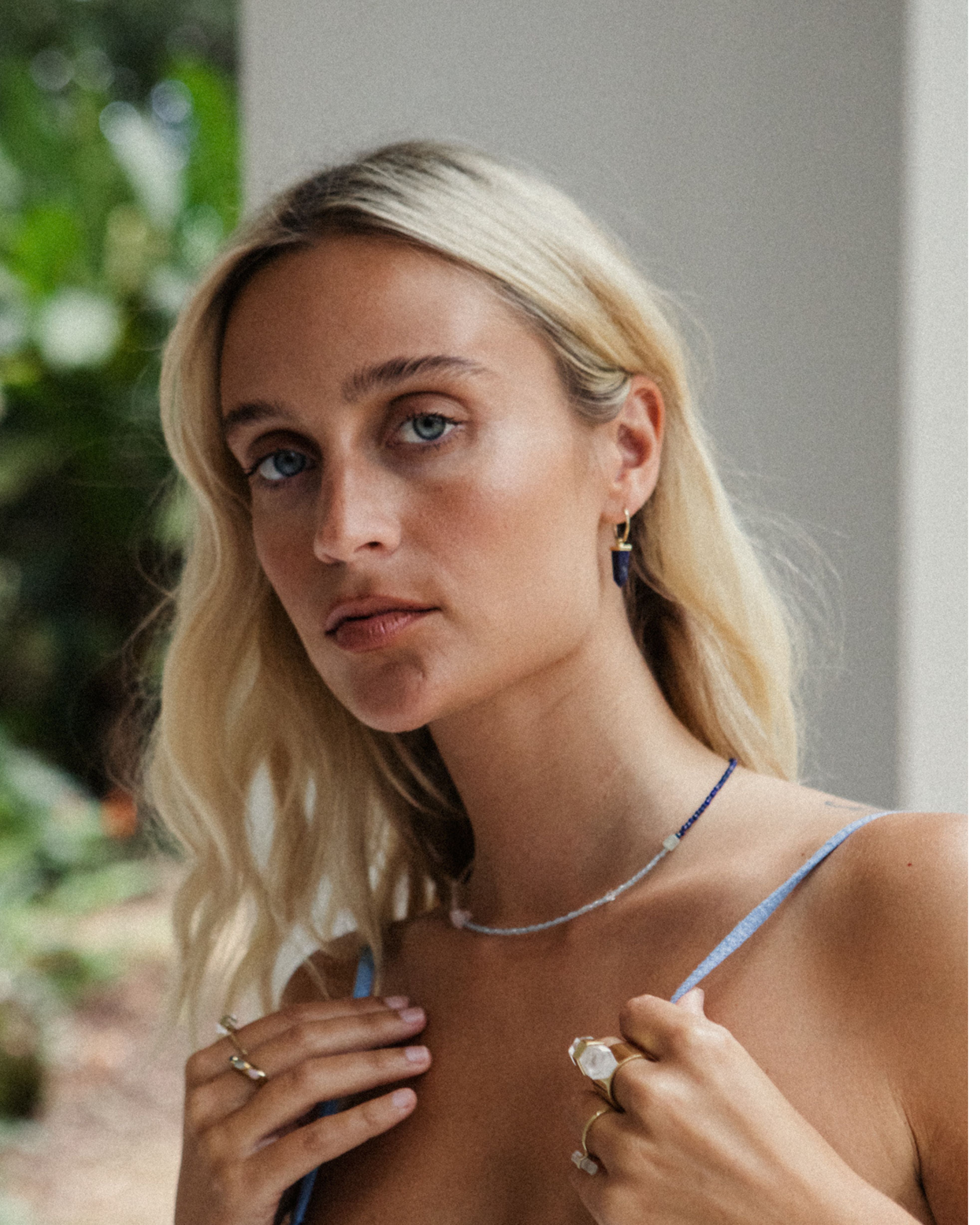 Woman with blonde hair wearing a necklace and rings outdoors