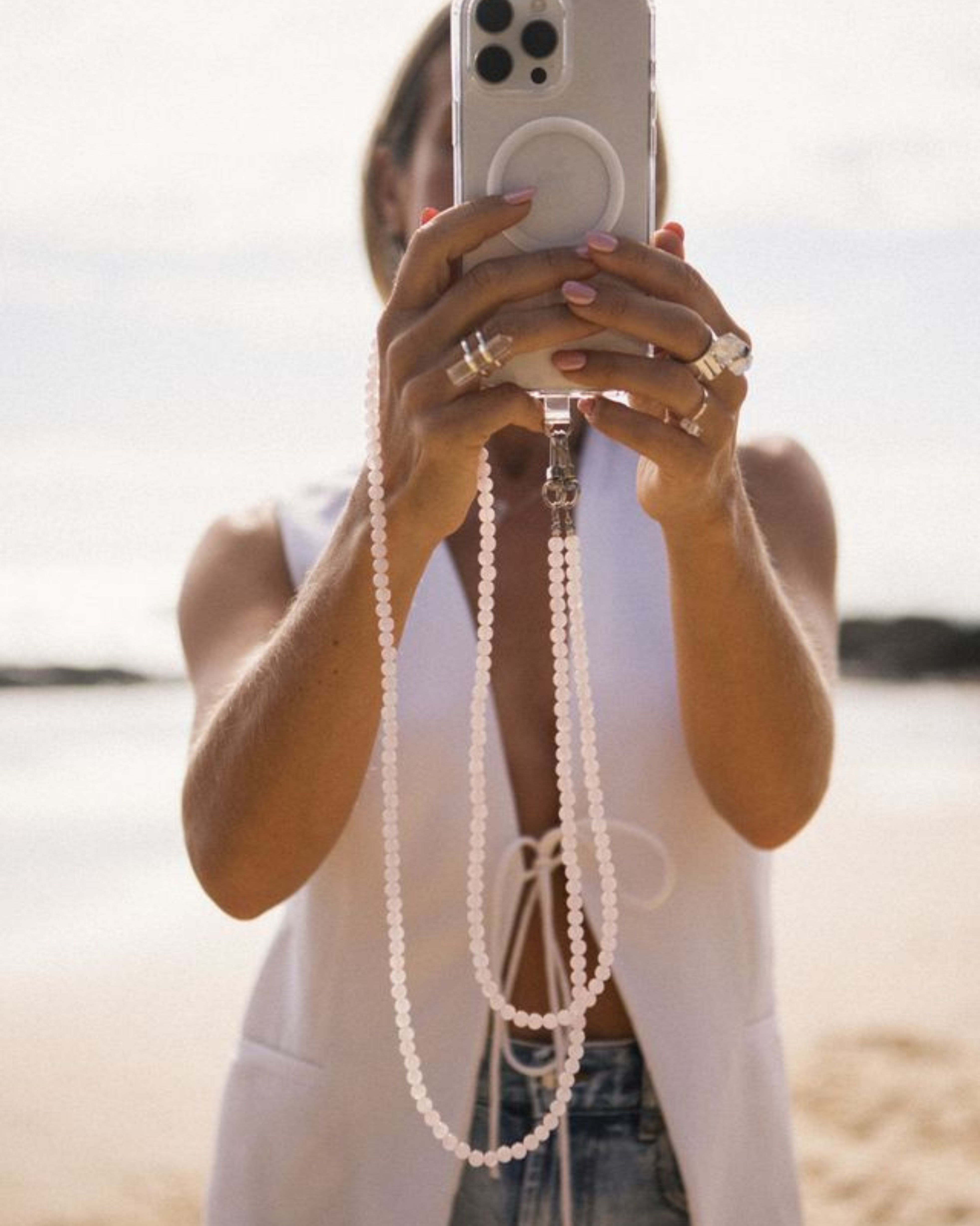 Person holding a phone with a beaded case on a beach