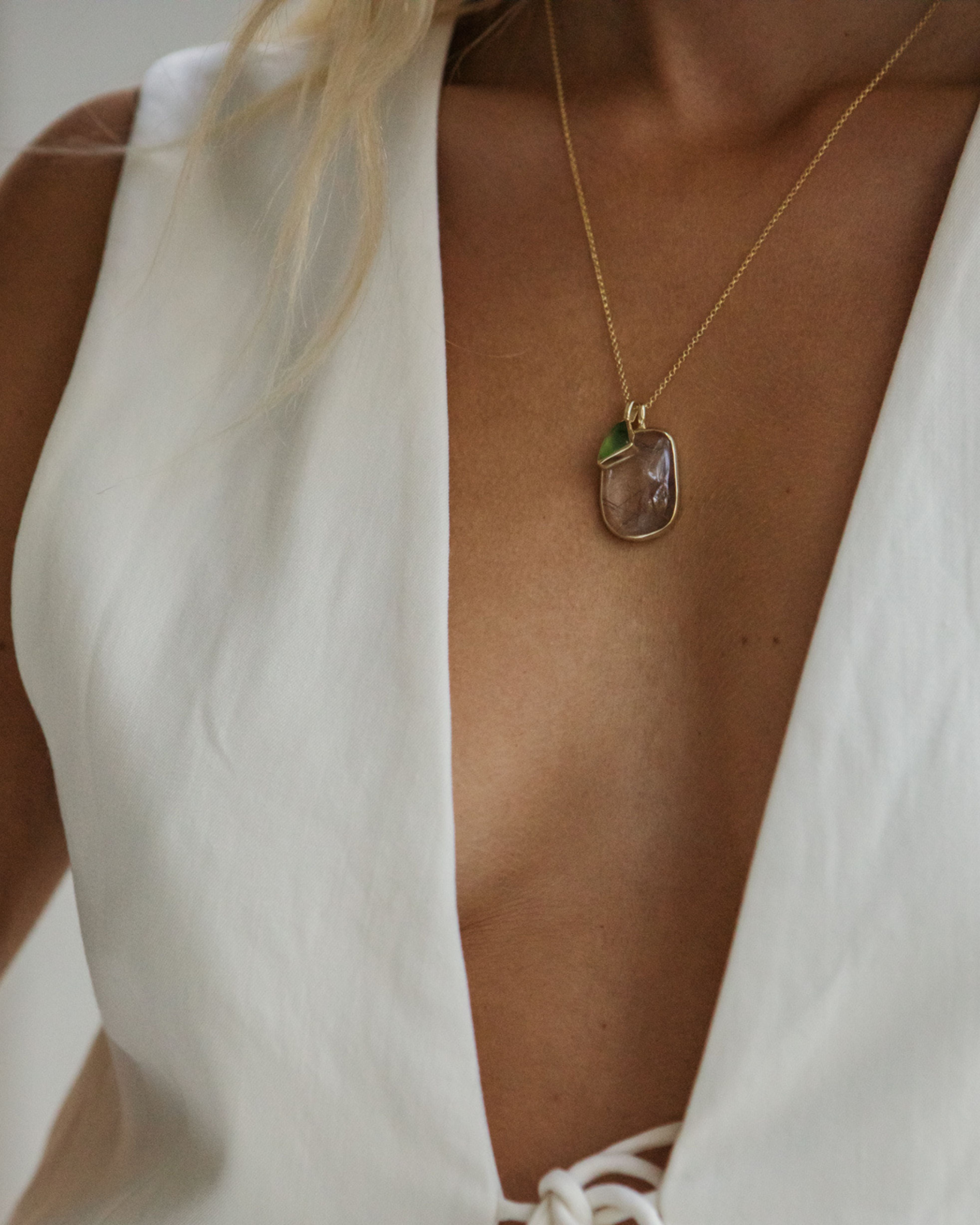 Close-up of a person wearing a gold necklace with a teardrop-shaped pendant with Ritulated Quartz + Peruvian Opal