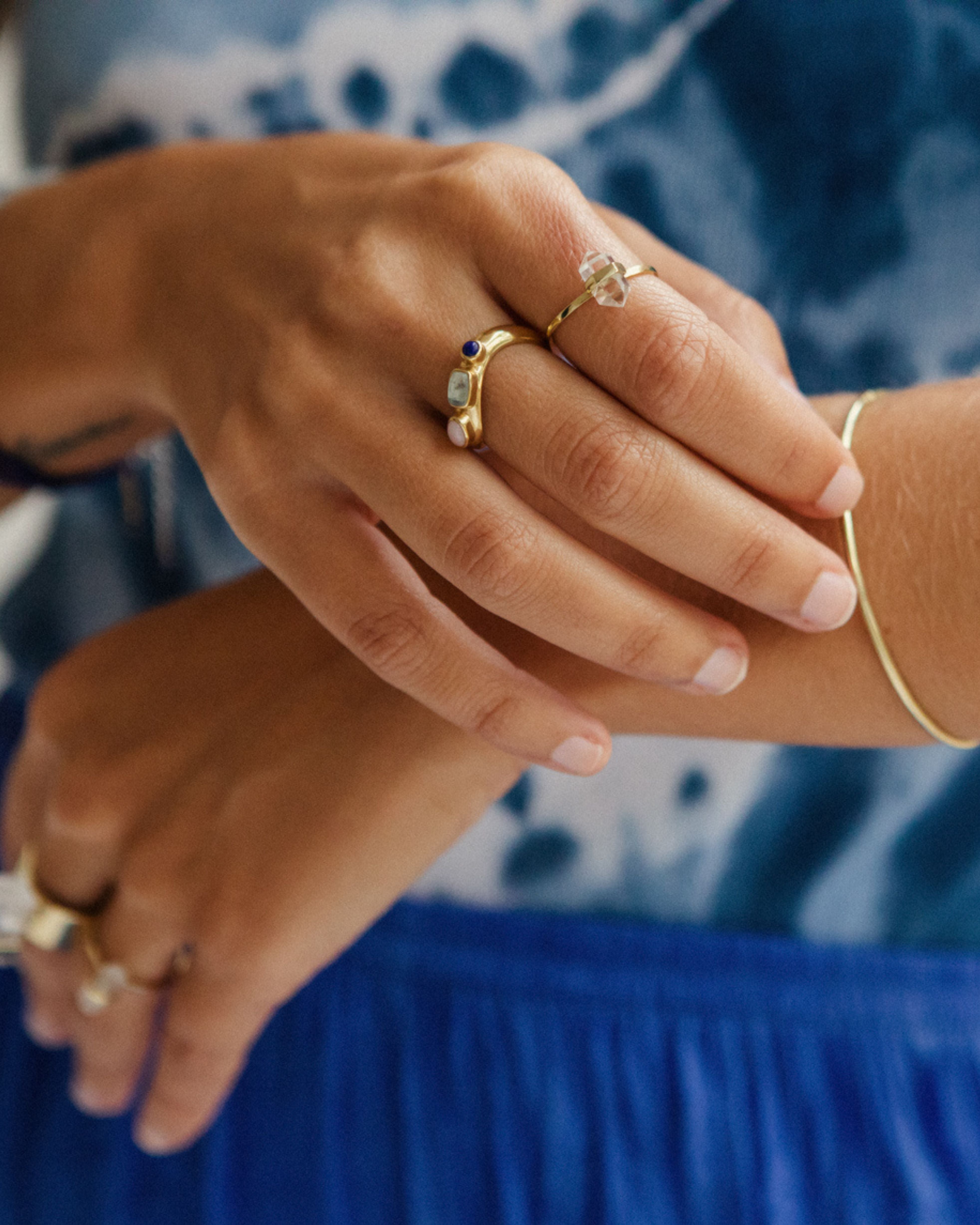 Close-up of hands wearing gold rings with gemstones against a blue fabric background