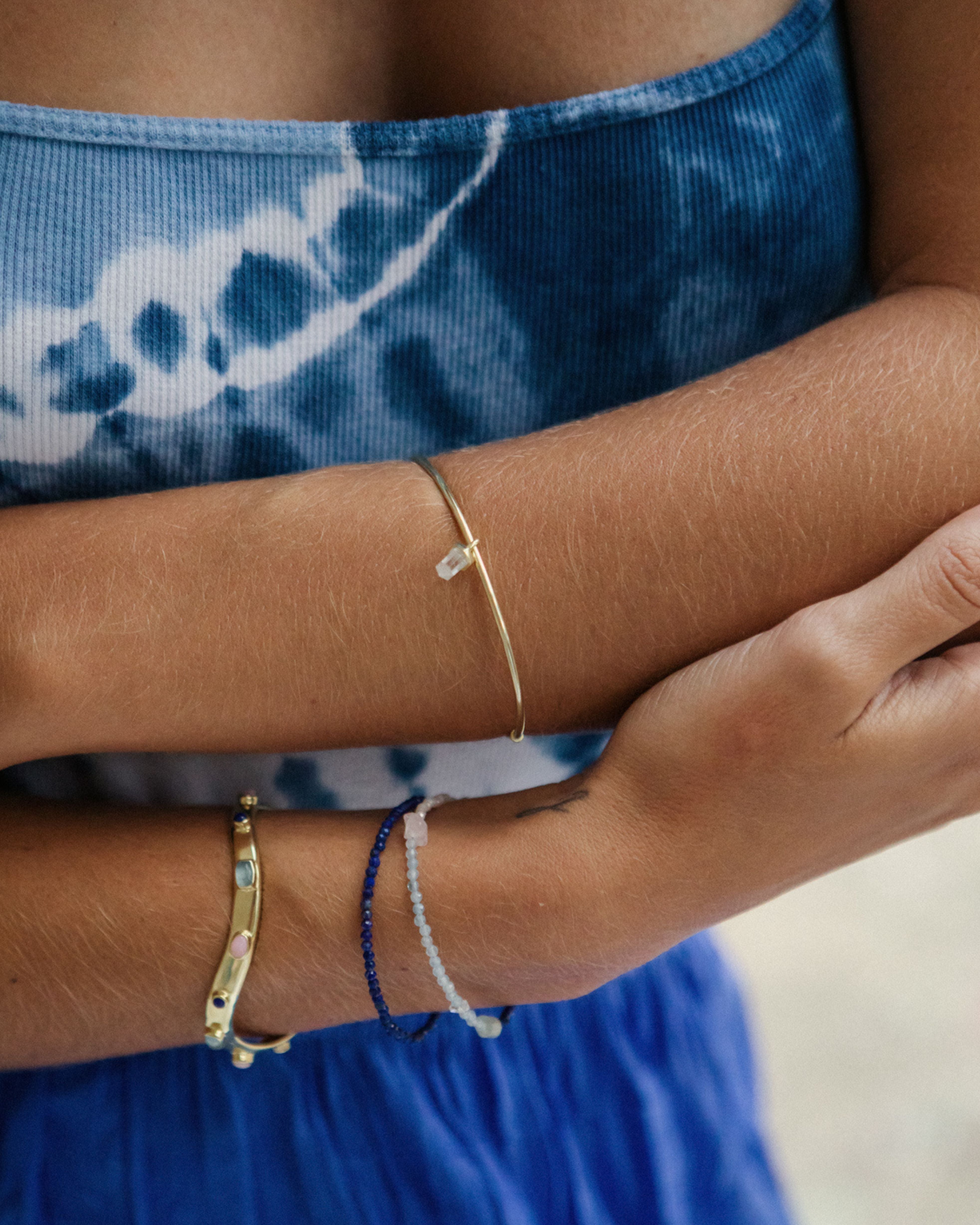Close-up of a person's arm wearing gold and beaded bracelets with a blue tie-dye garment.