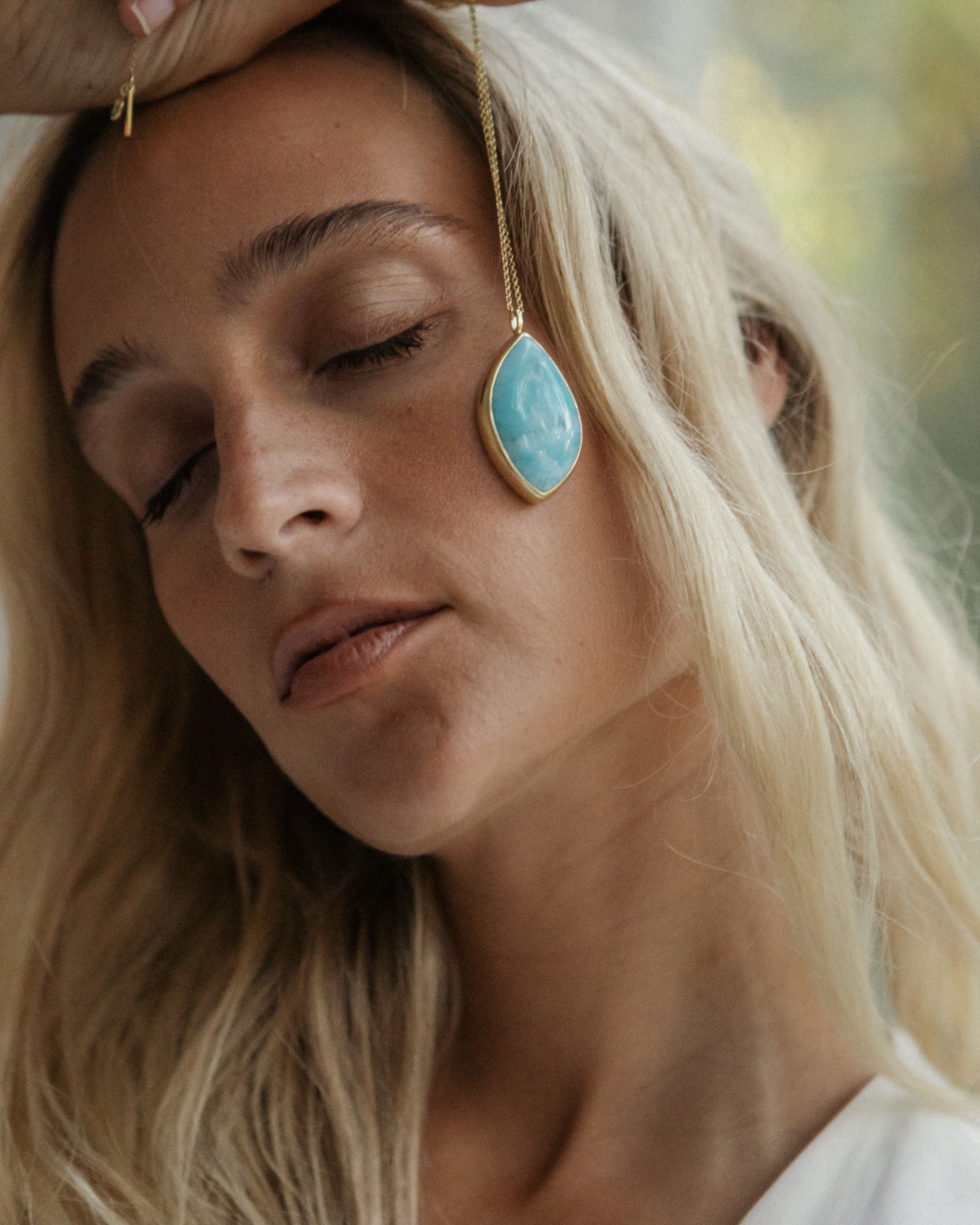 Close-up of a woman wearing a larimar teardrop earring with a blurred background
