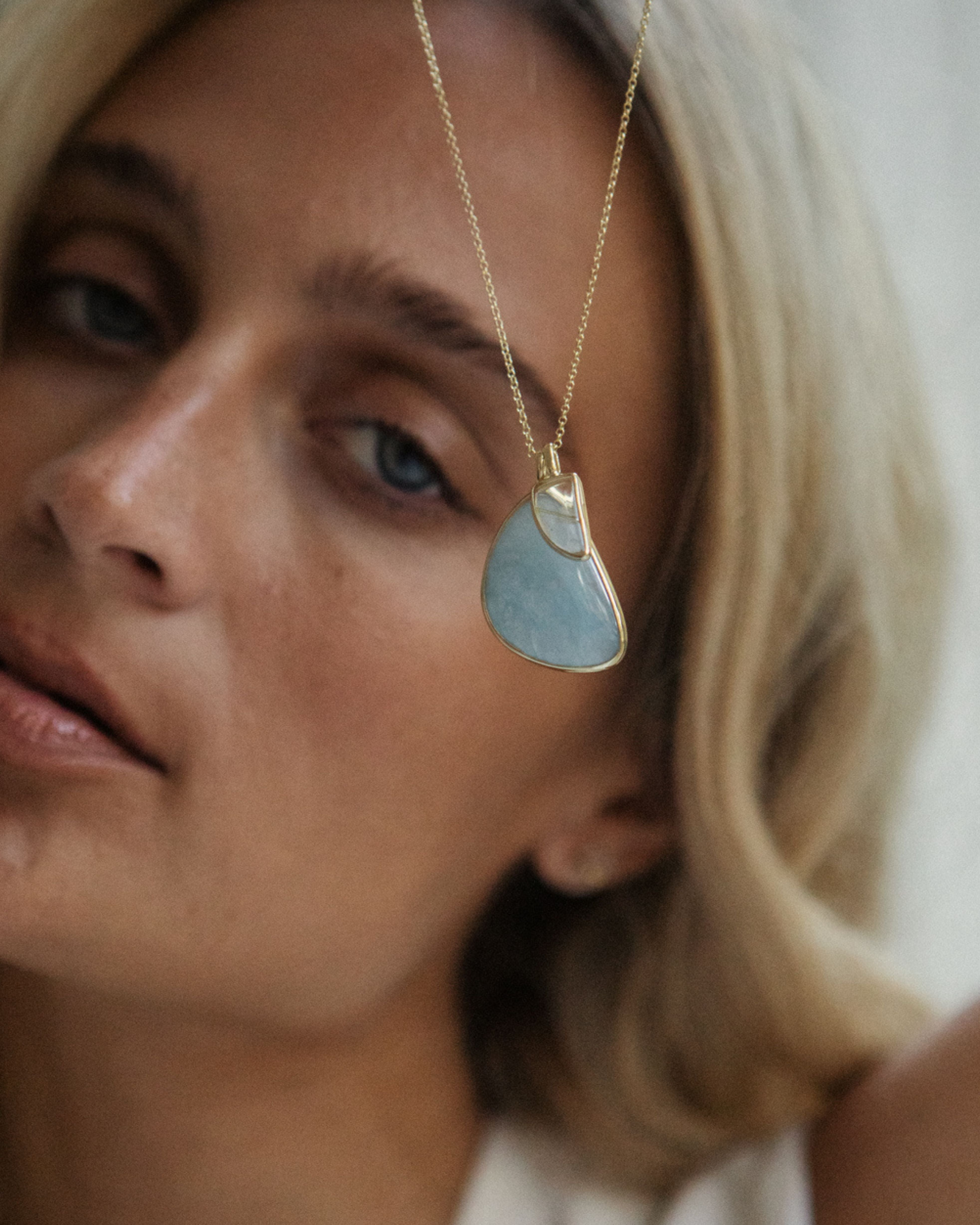Close-up of a woman wearing a gold necklace with a Larimar + Rutilated Quartz pendant.