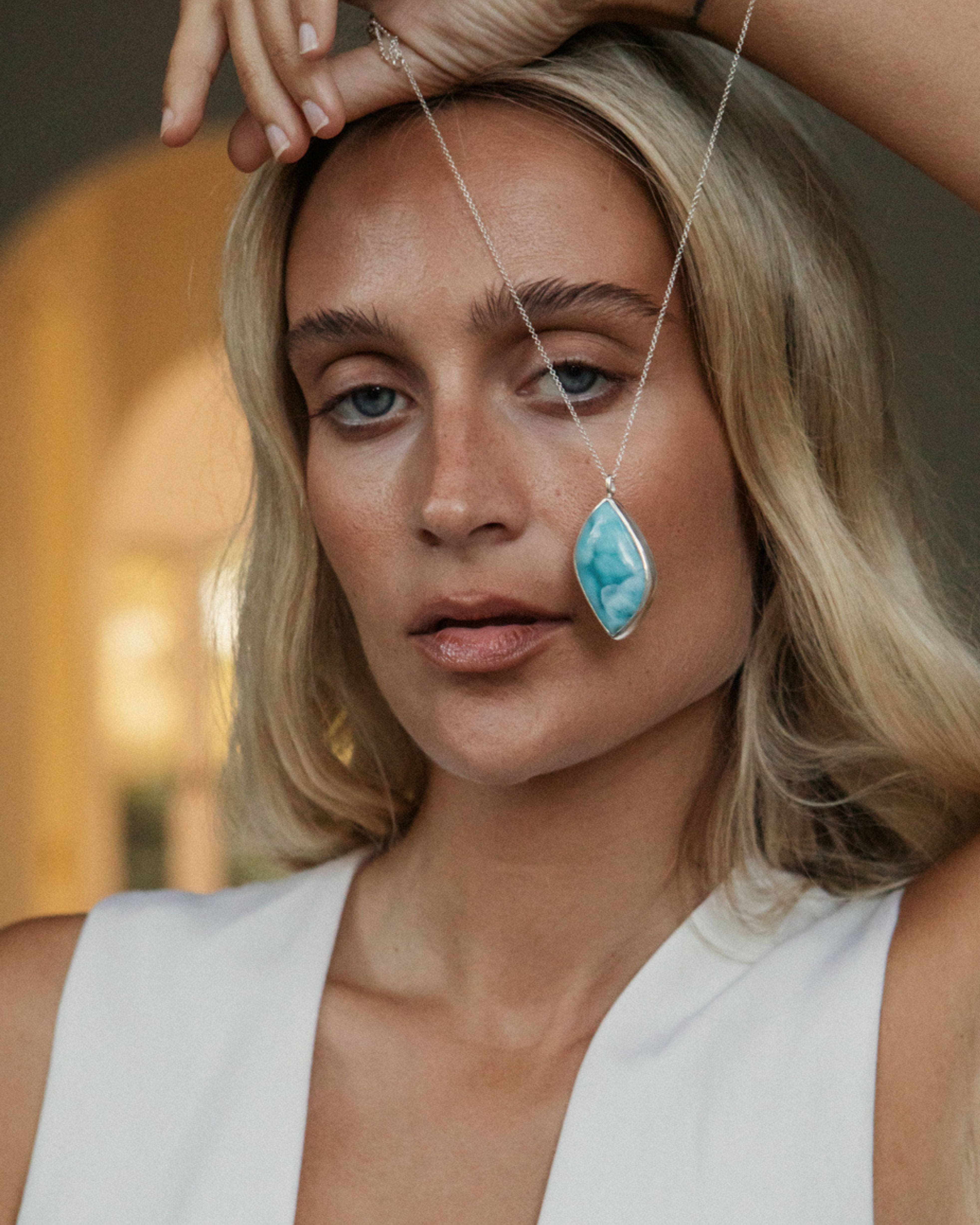 Woman wearing a necklace with a Larimar pendant, set against a blurred indoor background.