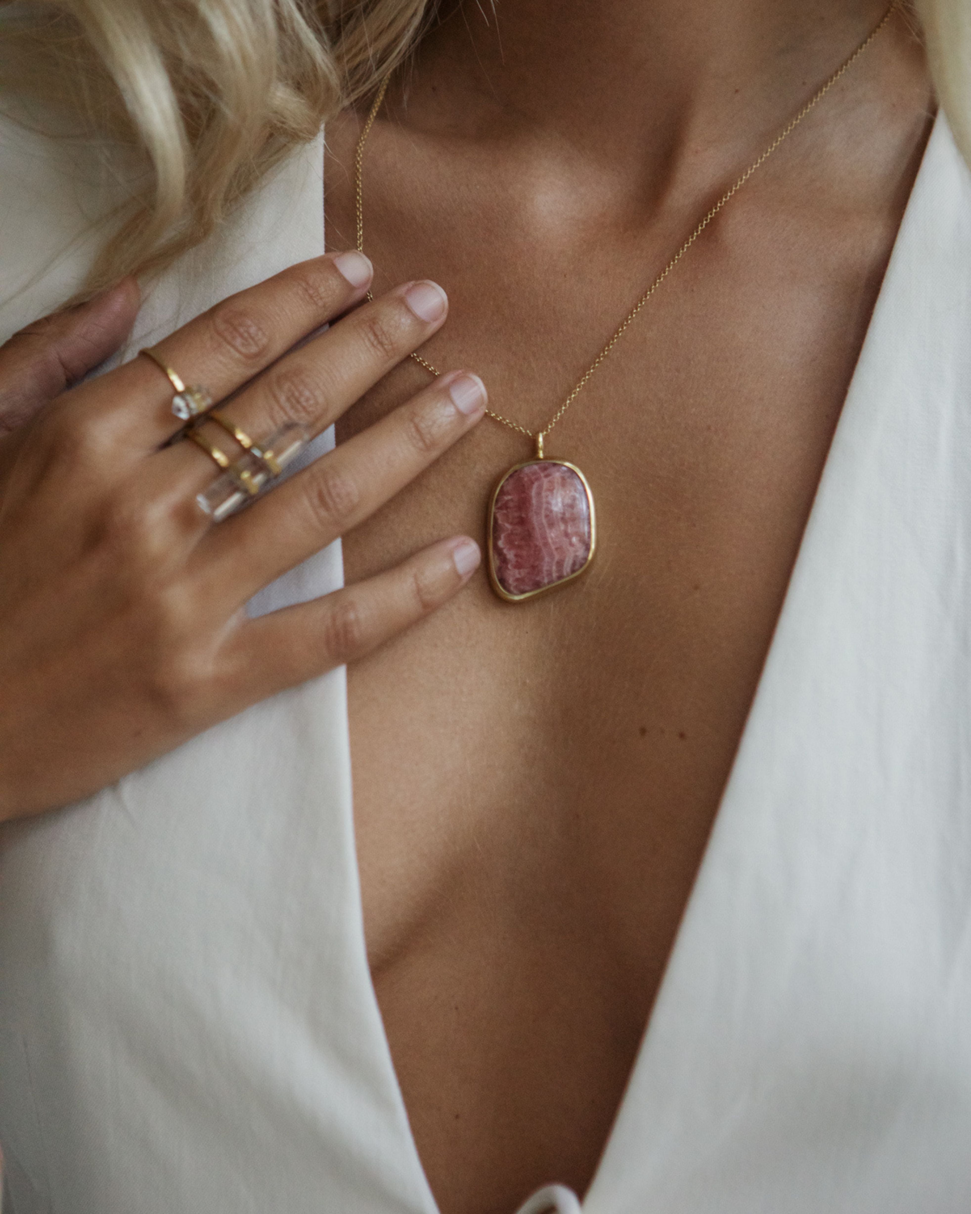 Close-up of a necklace with a Rhodochrosite pendant worn by a person in a white outfit.