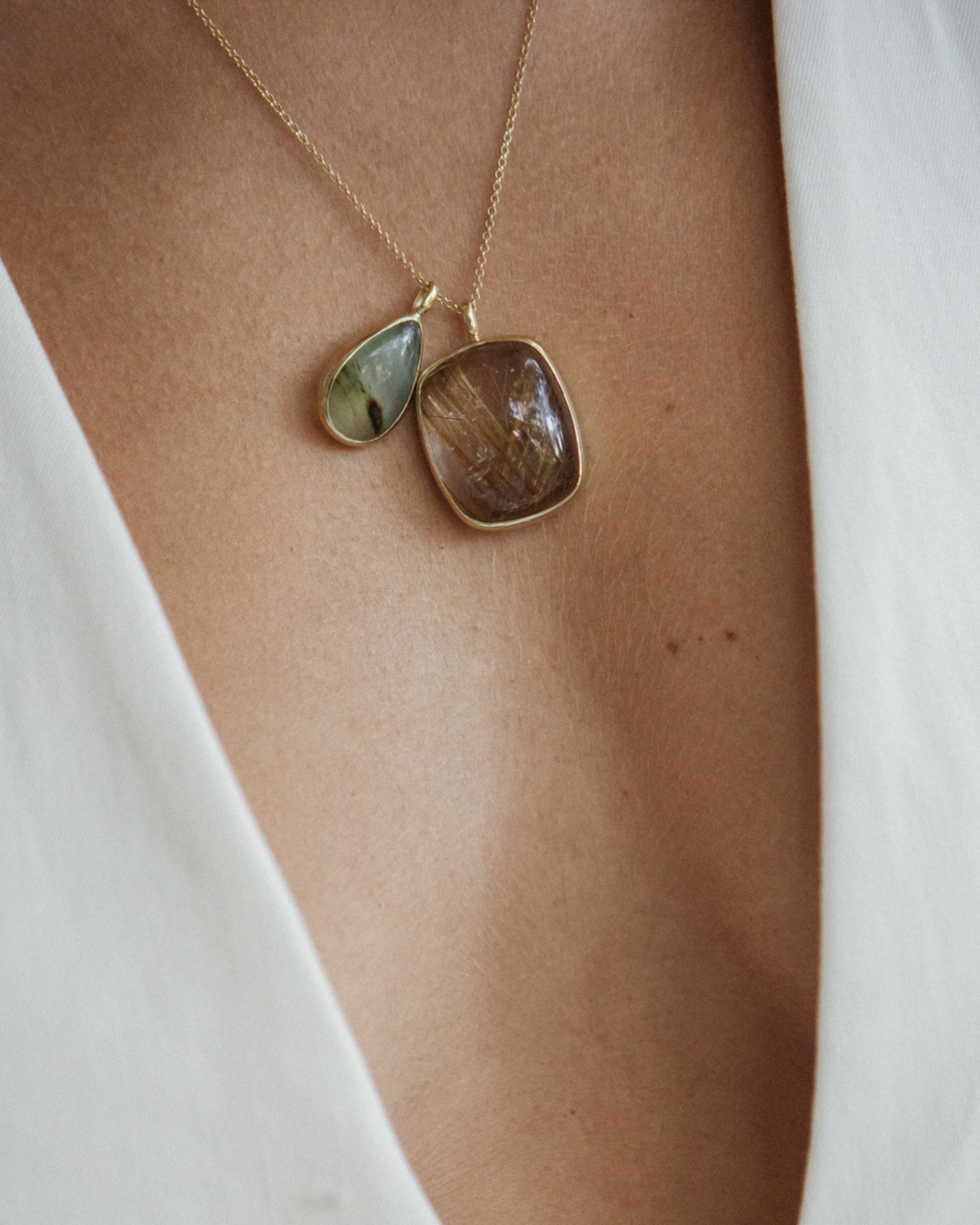 Close-up of a person wearing a gold necklace with a teardrop-shaped pendant with Ritulated Quartz + Peruvian Opal
