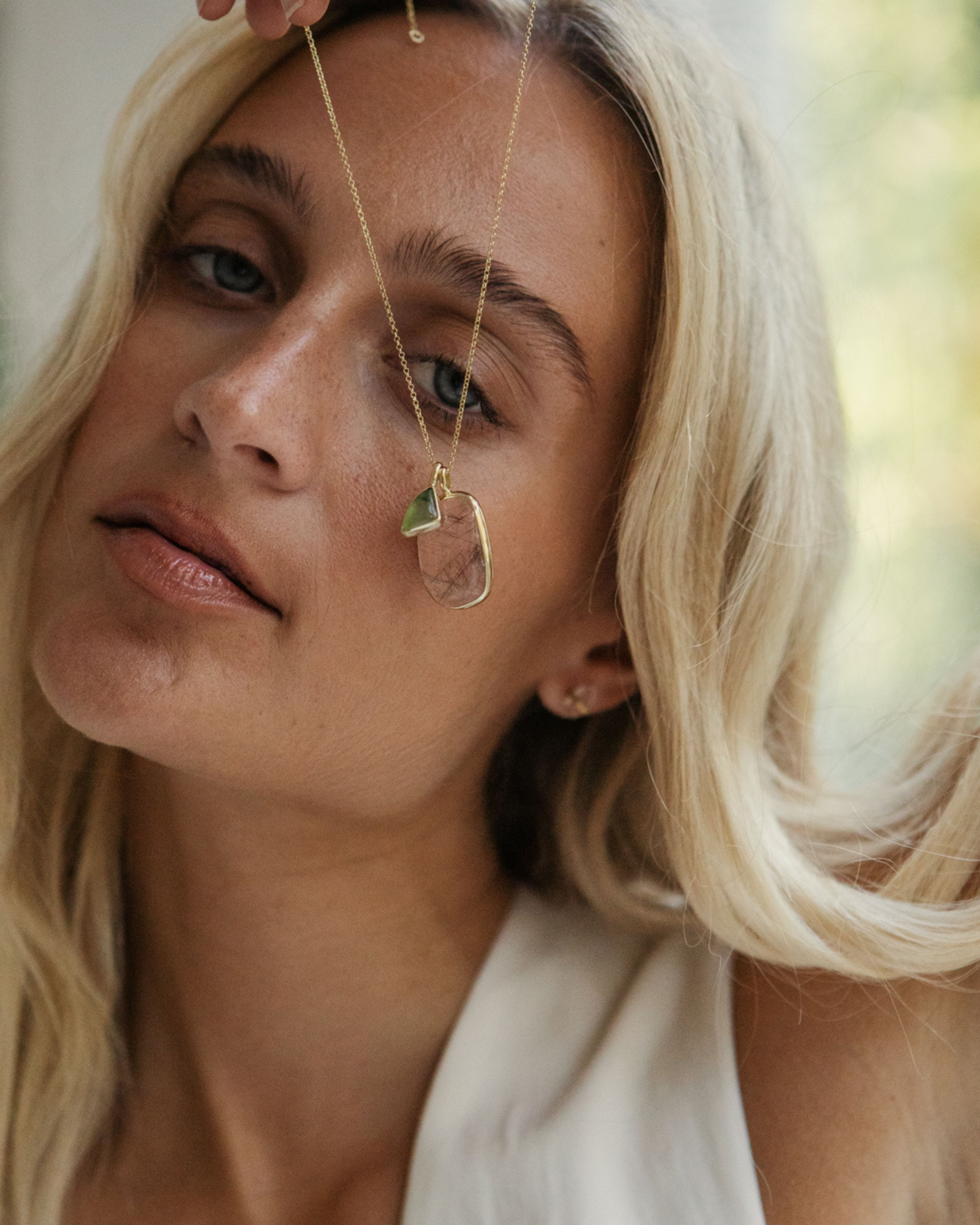 Close-up of a person wearing a gold necklace with a teardrop-shaped pendant with Ritulated Quartz + Peruvian Opal