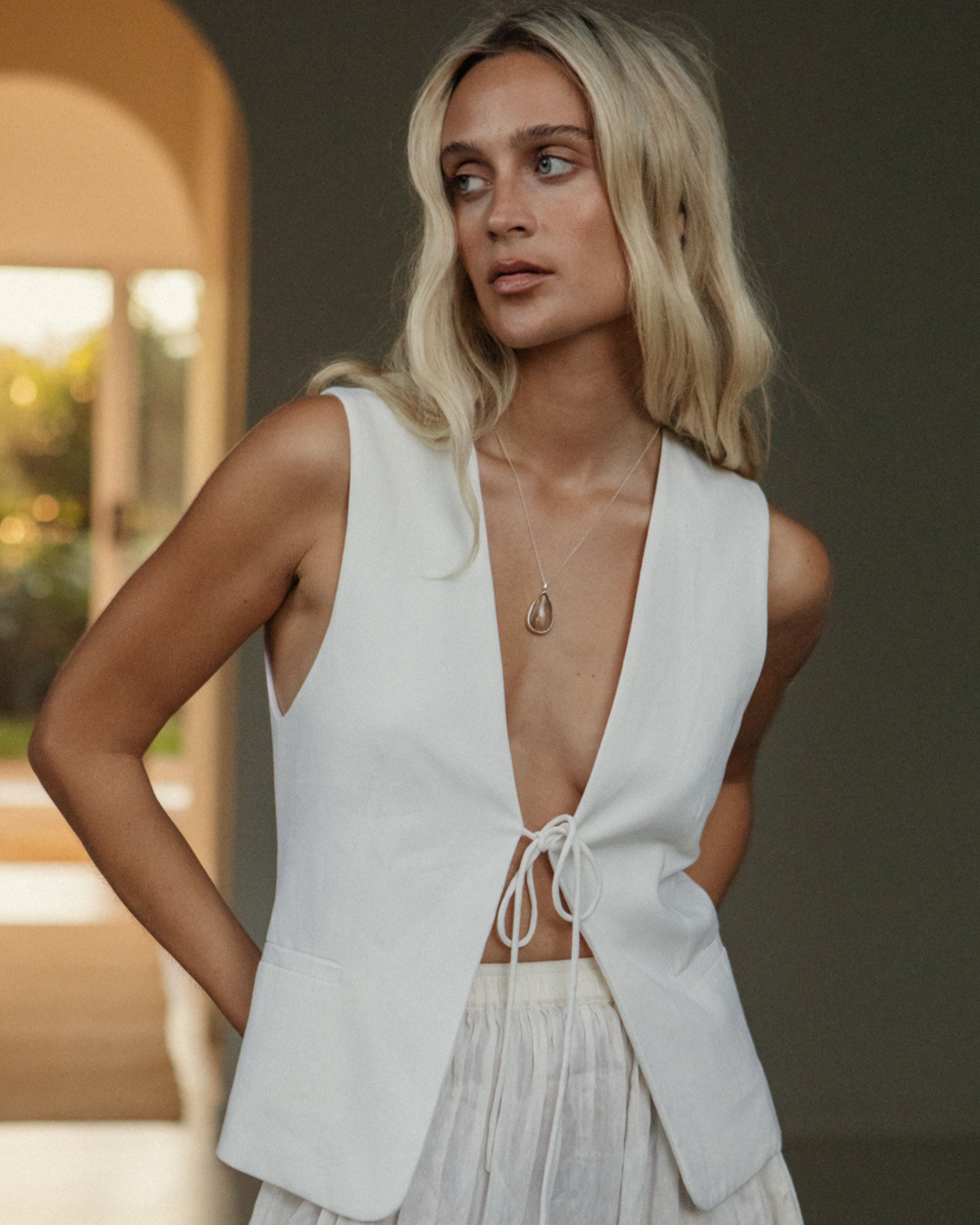 Woman wearing a white sleeveless top with a deep neckline and a matching skirt. with Rutilated Quartz necklace.